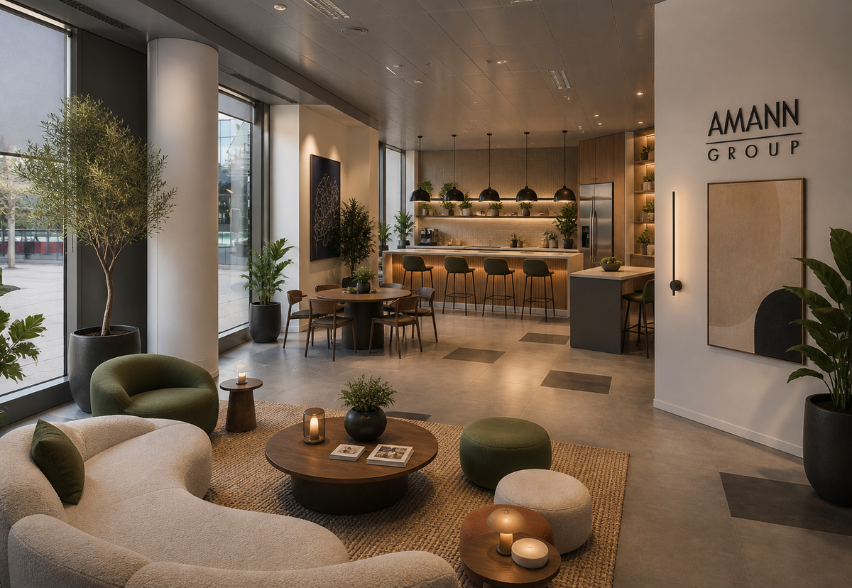 Office social space with sofas, plants and a coffee area for informal meetings, featuring the AMANN GROUP logo.